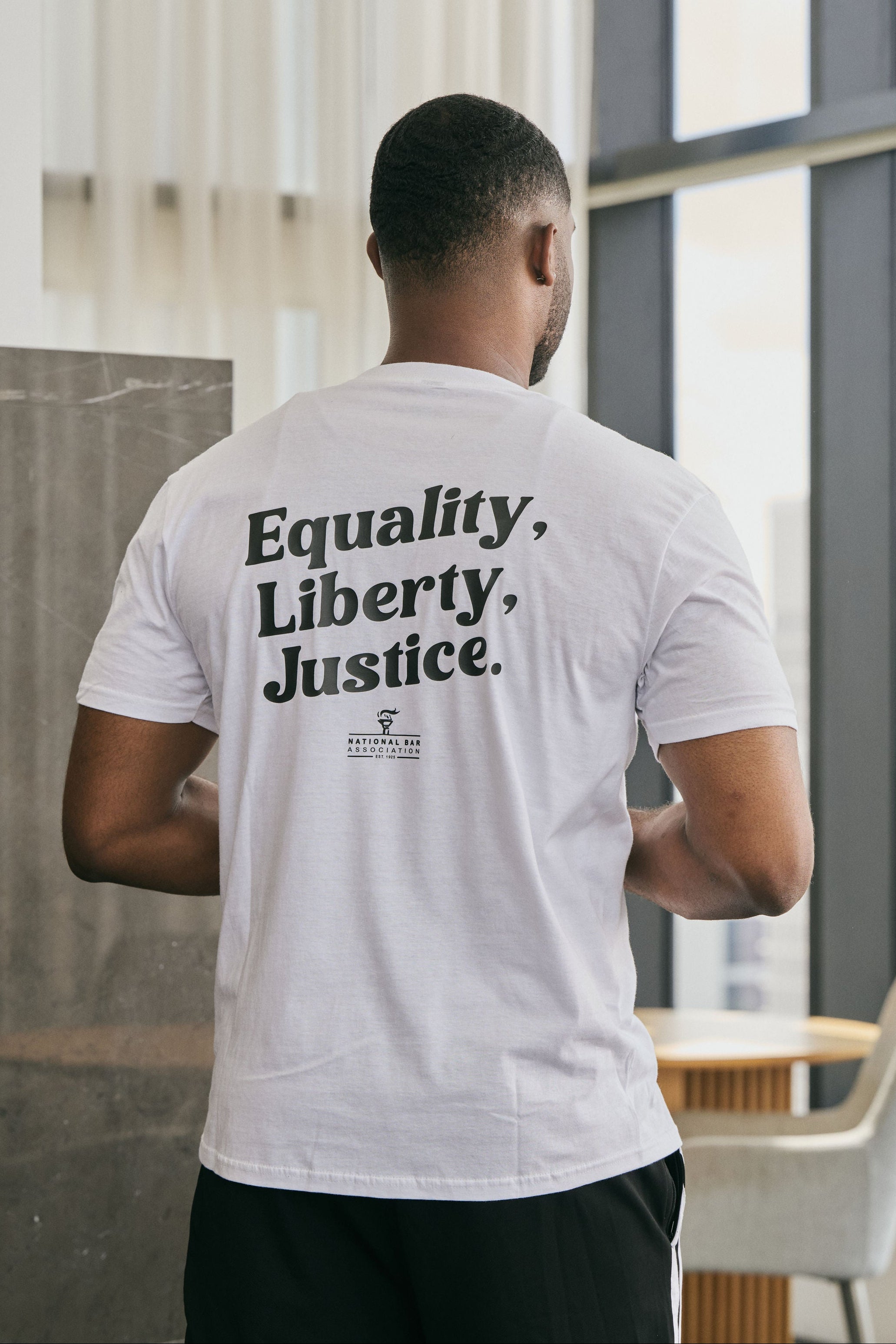 Person wearing a white t-shirt with 'Equality, Liberty, Justice' text on the back in an indoor setting.