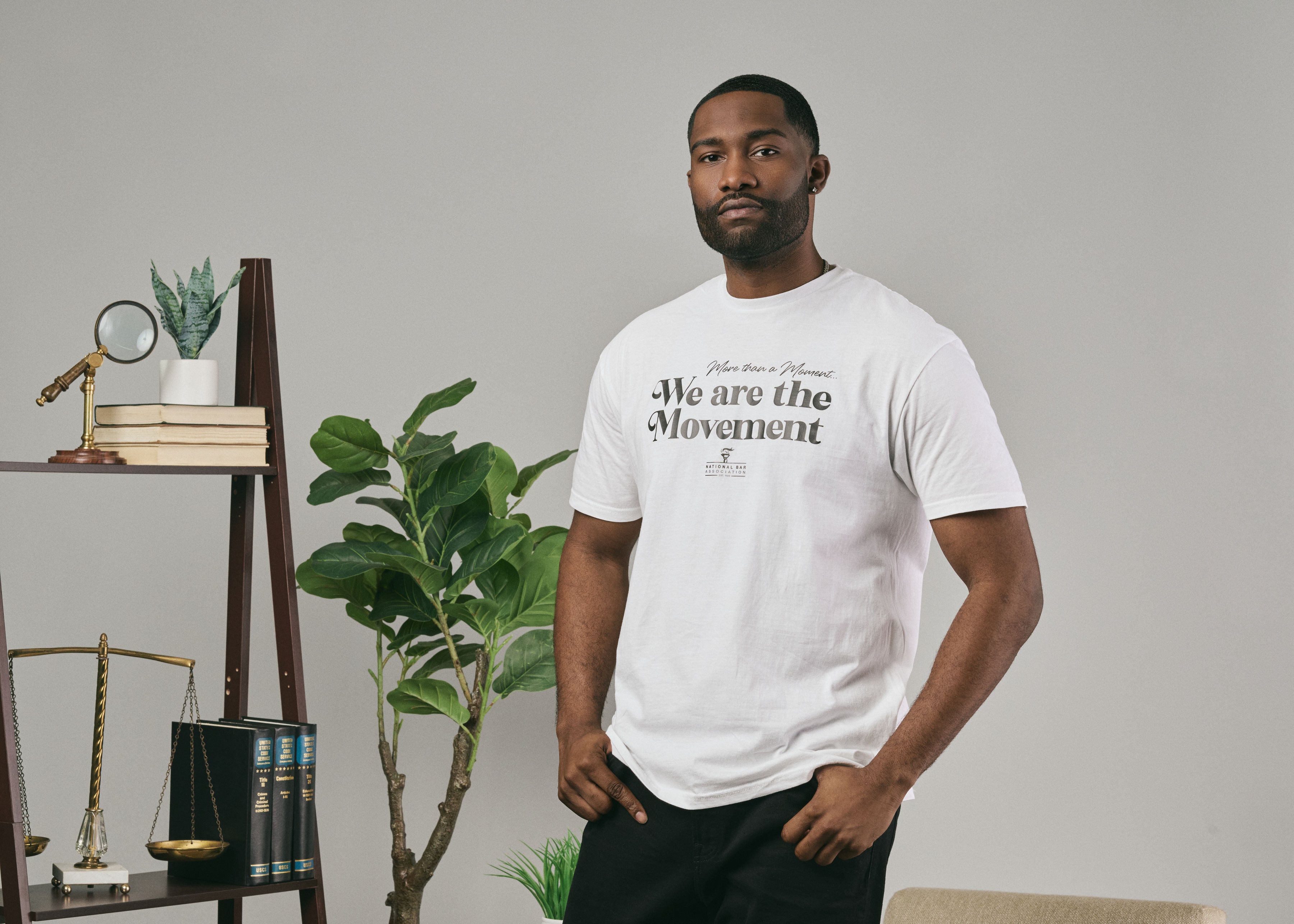 Man wearing a white t-shirt with text in a room with plants and books.