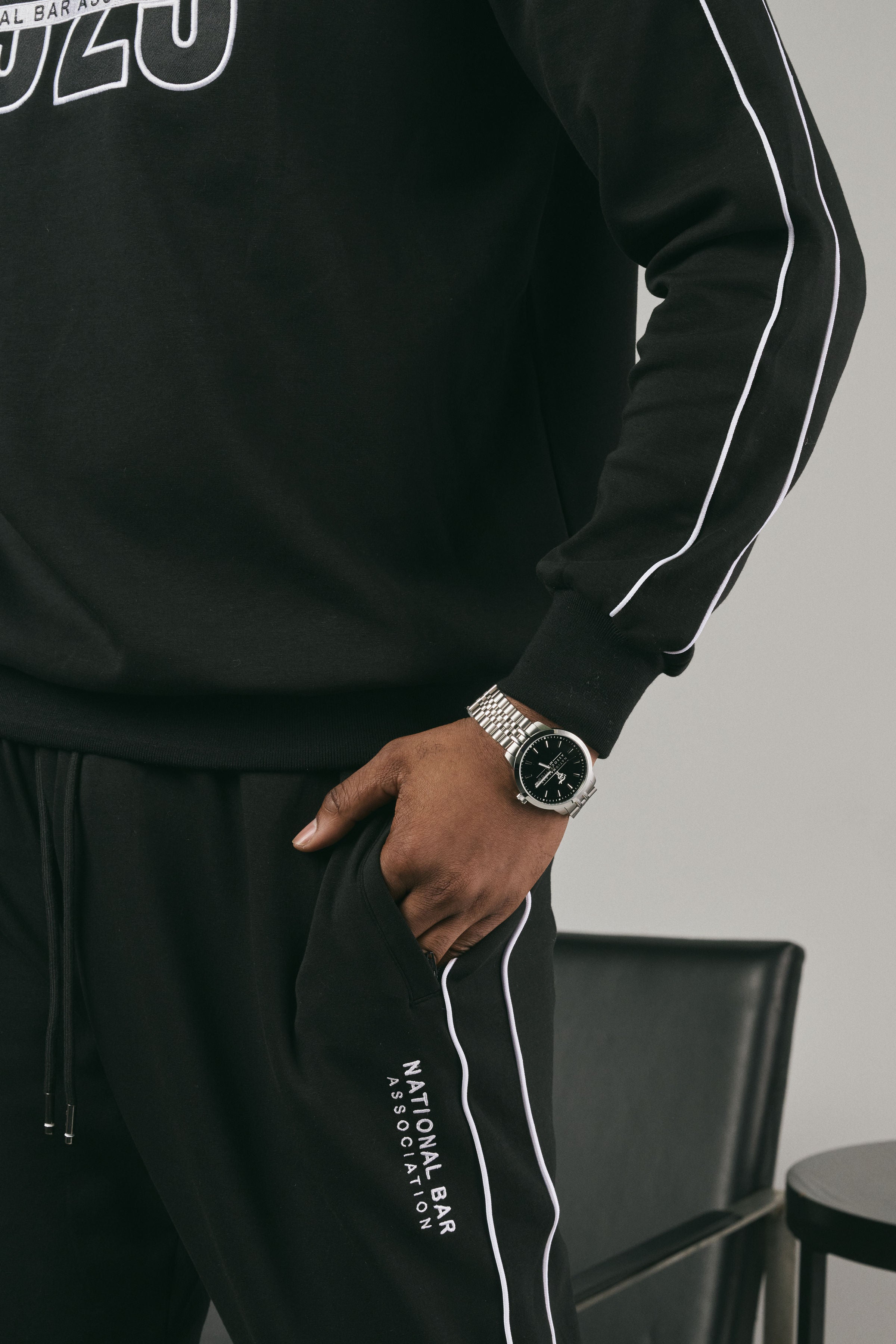 Person wearing a black sweatshirt and black joggers with white piping on a grey background