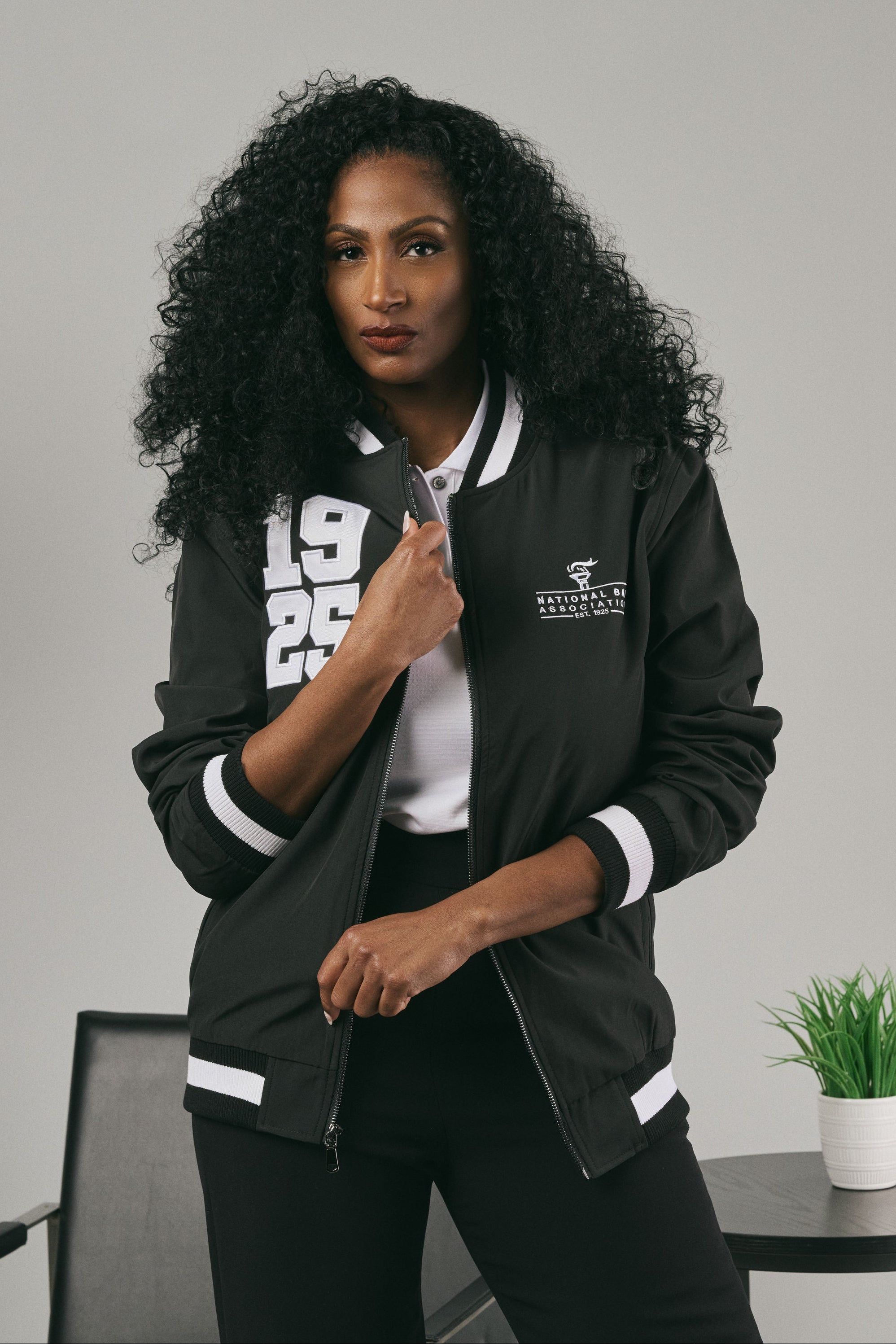 Woman wearing a black jacket with white accents, standing against a grey background.