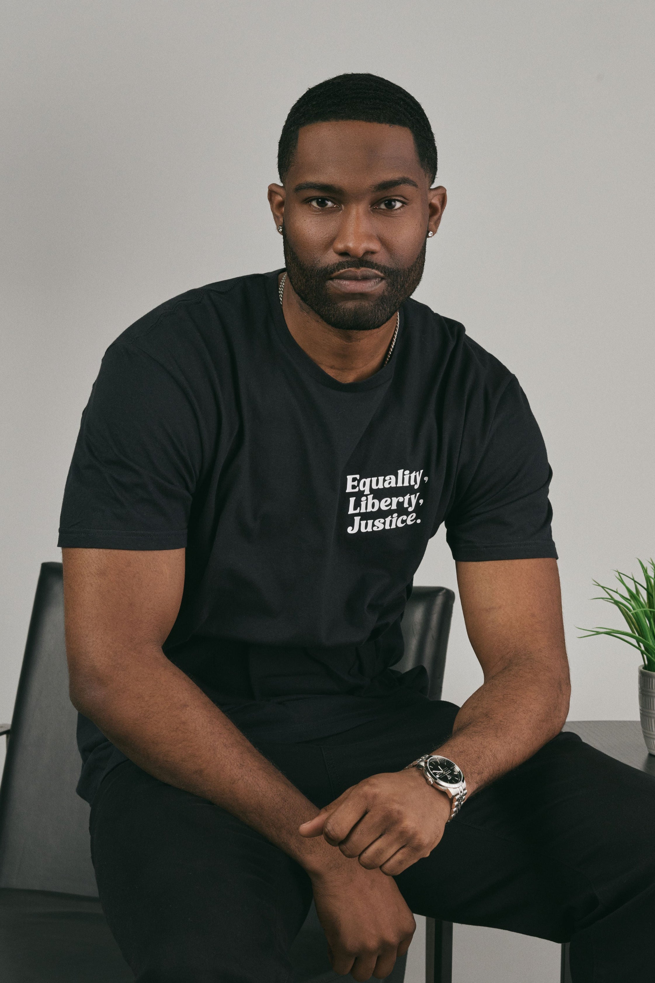 Man wearing a black t-shirt with text 'Equality, Liberty, Justice.' sitting against a plain background