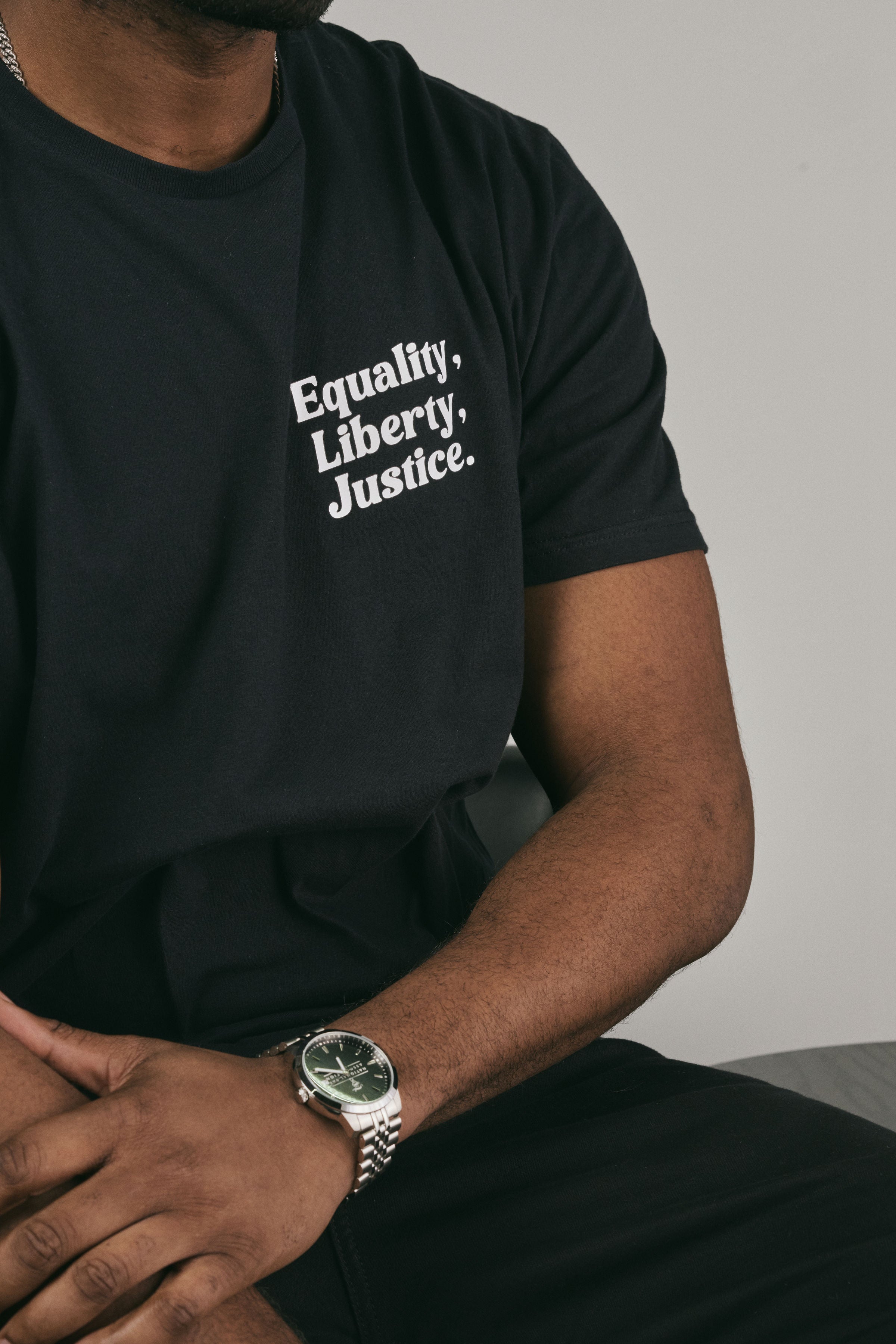 Person wearing a black t-shirt with 'Equality, Liberty, Justice.' text, sitting against a neutral background.