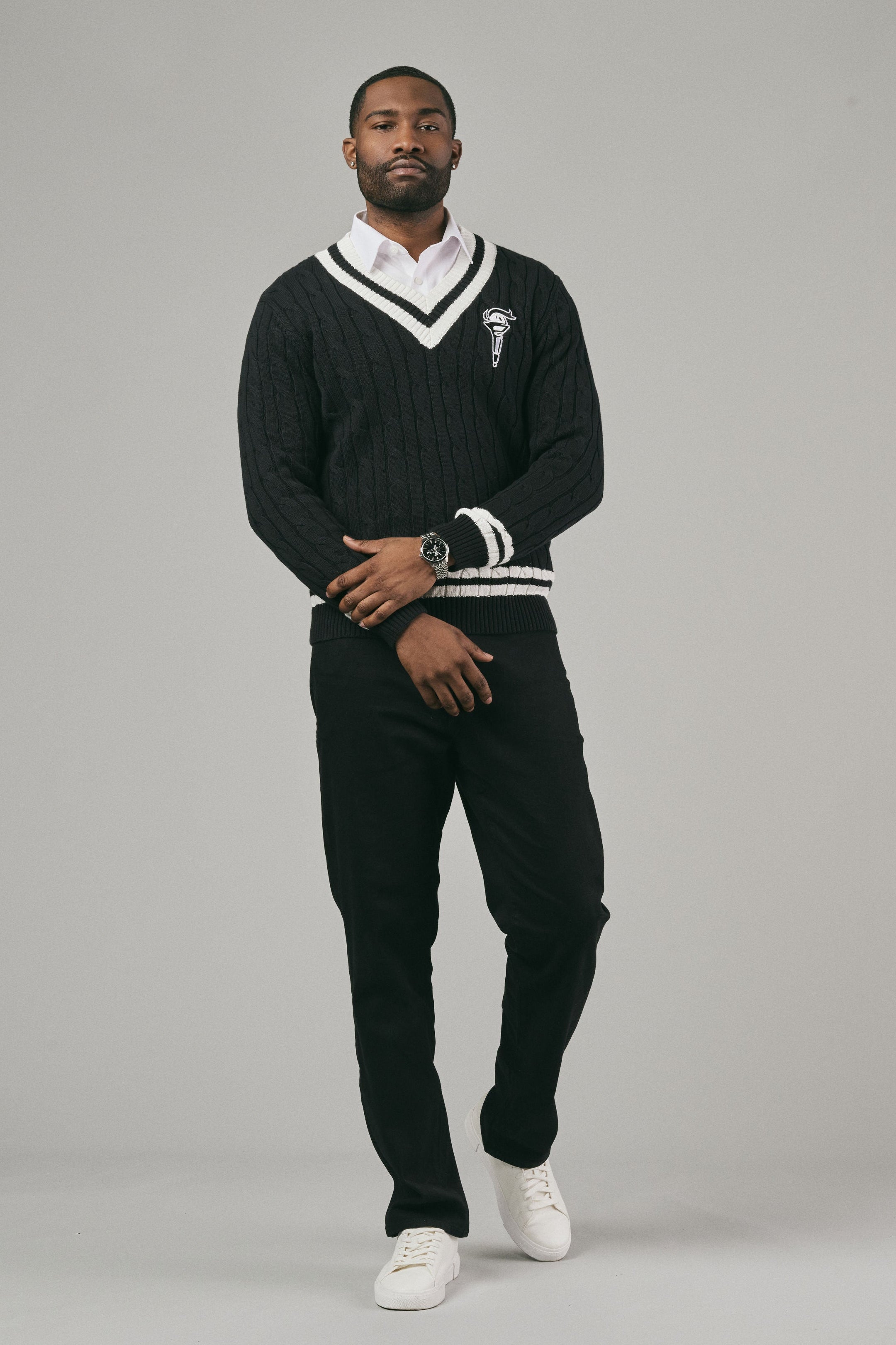 Man wearing a black sweater with white trim and pants on a grey background