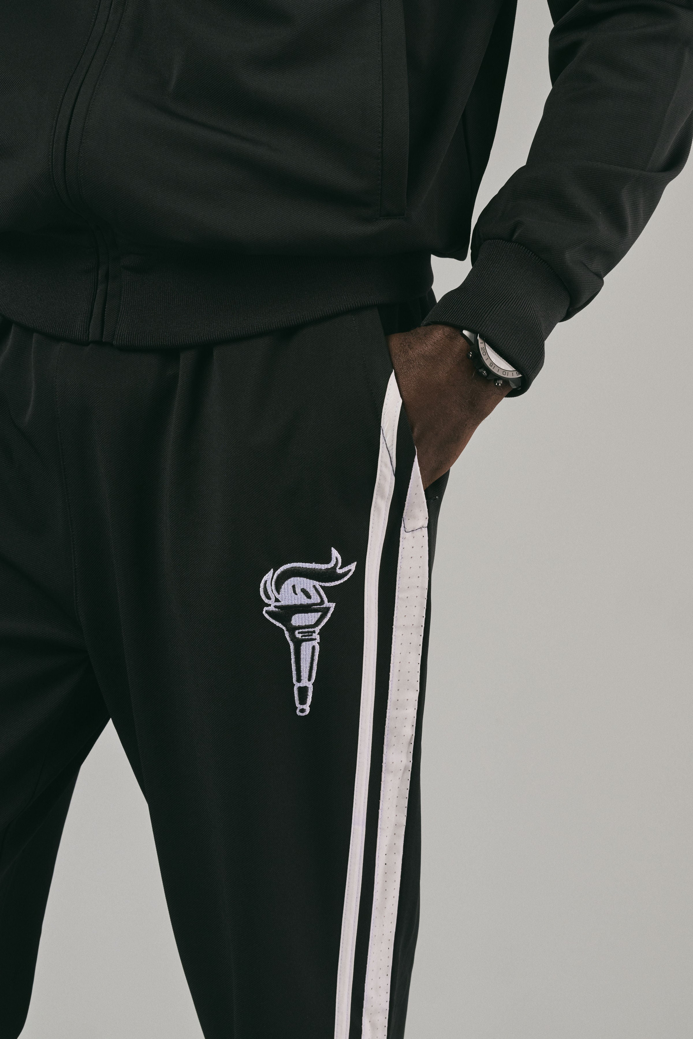 Close up of black track pants with a white logo on grey background