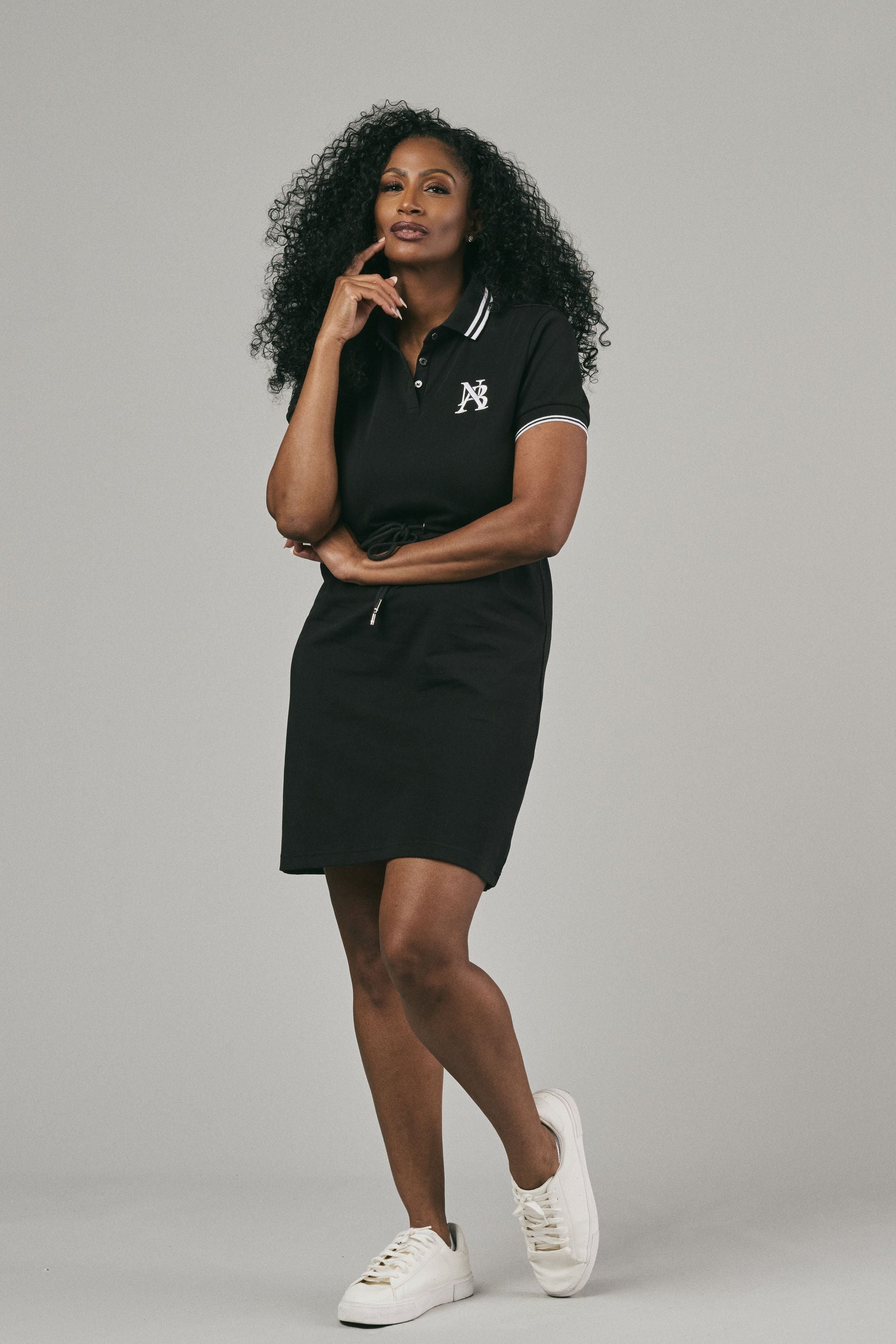 Woman wearing a black polo dress with a logo posing against a grey background