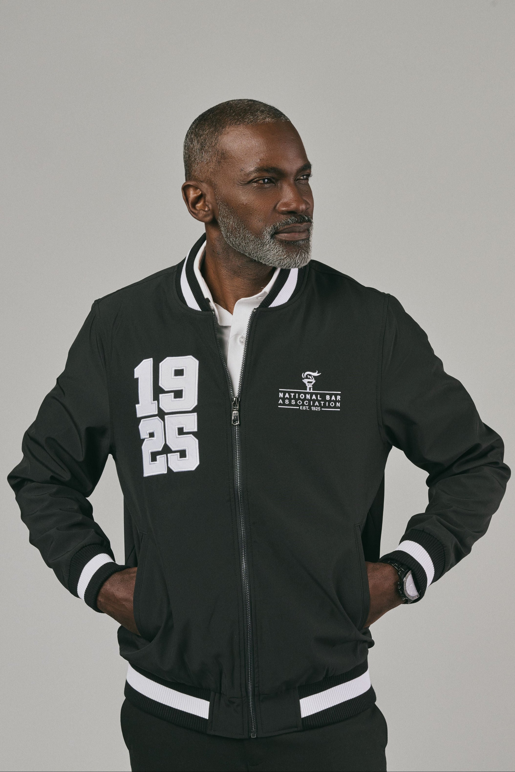 Man wearing a black jacket with white text and '1925' on a grey background