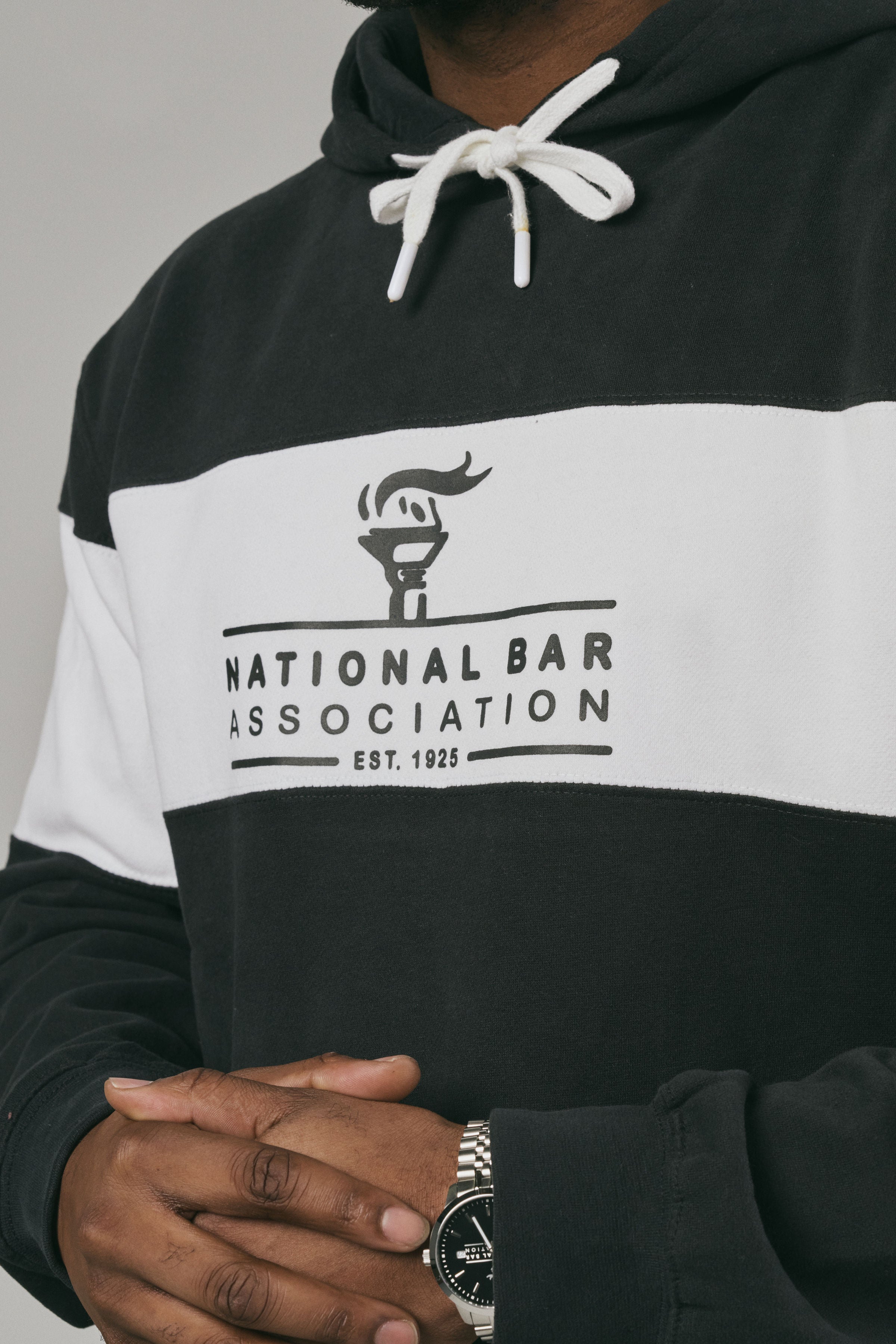 Close up of a person wearing a black and white hoodie with 'National Bar Association' logo on a grey background