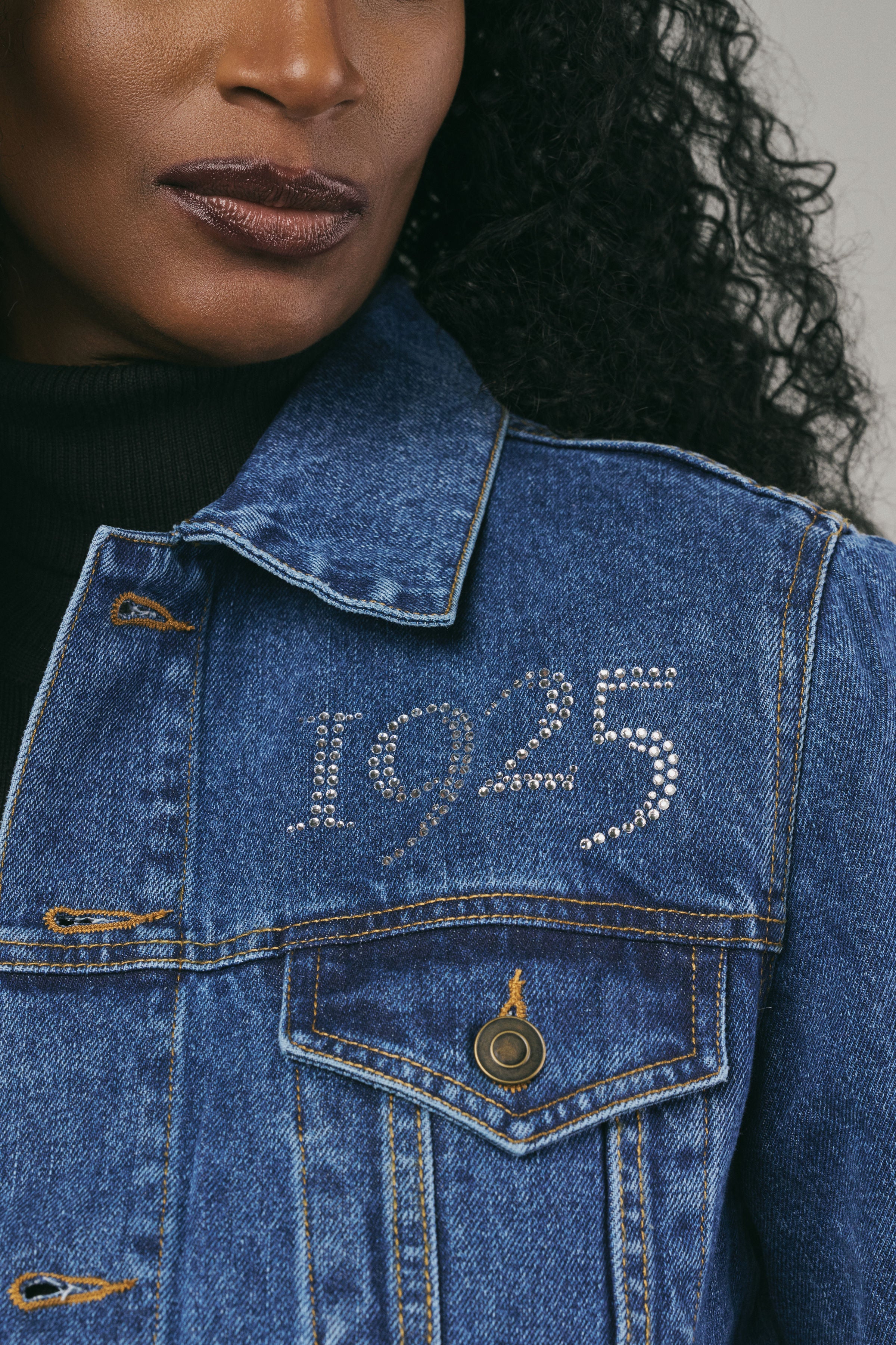 Close-up of a person wearing a blue denim jacket with '1925' embroidery.