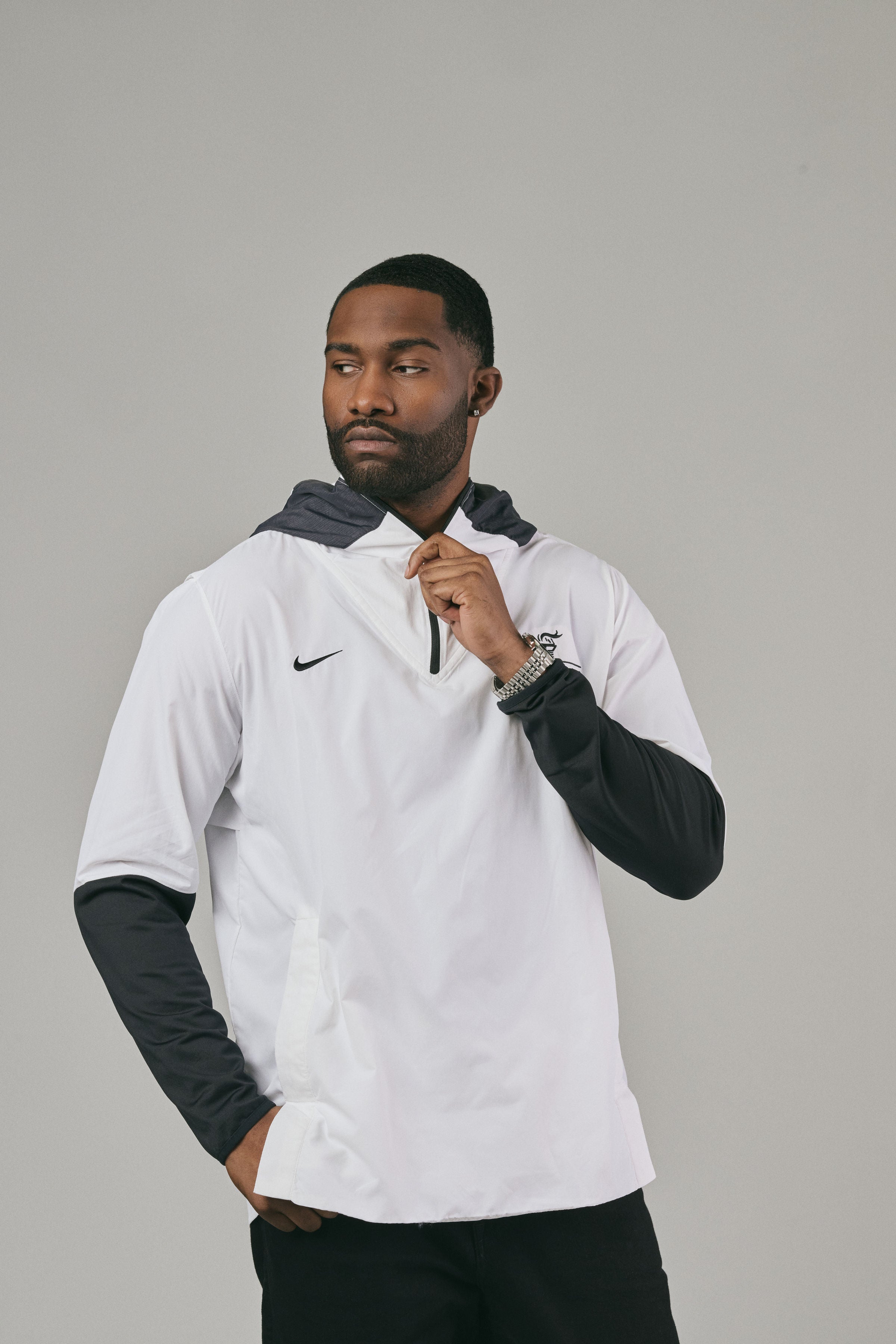 Man wearing a white jacket with a brand logo looking sideways against a grey background