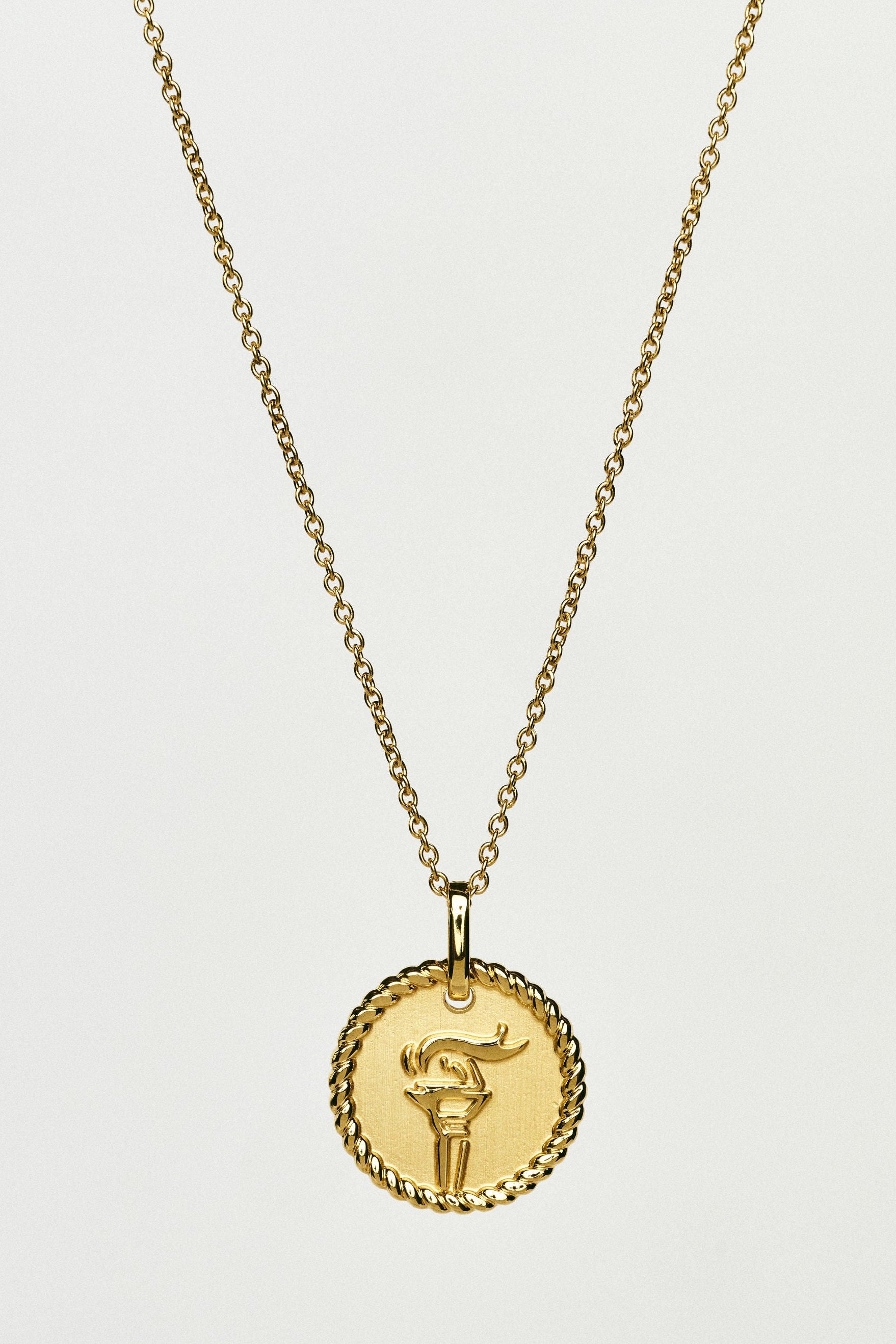 Gold necklace with a round pendant on a light grey background