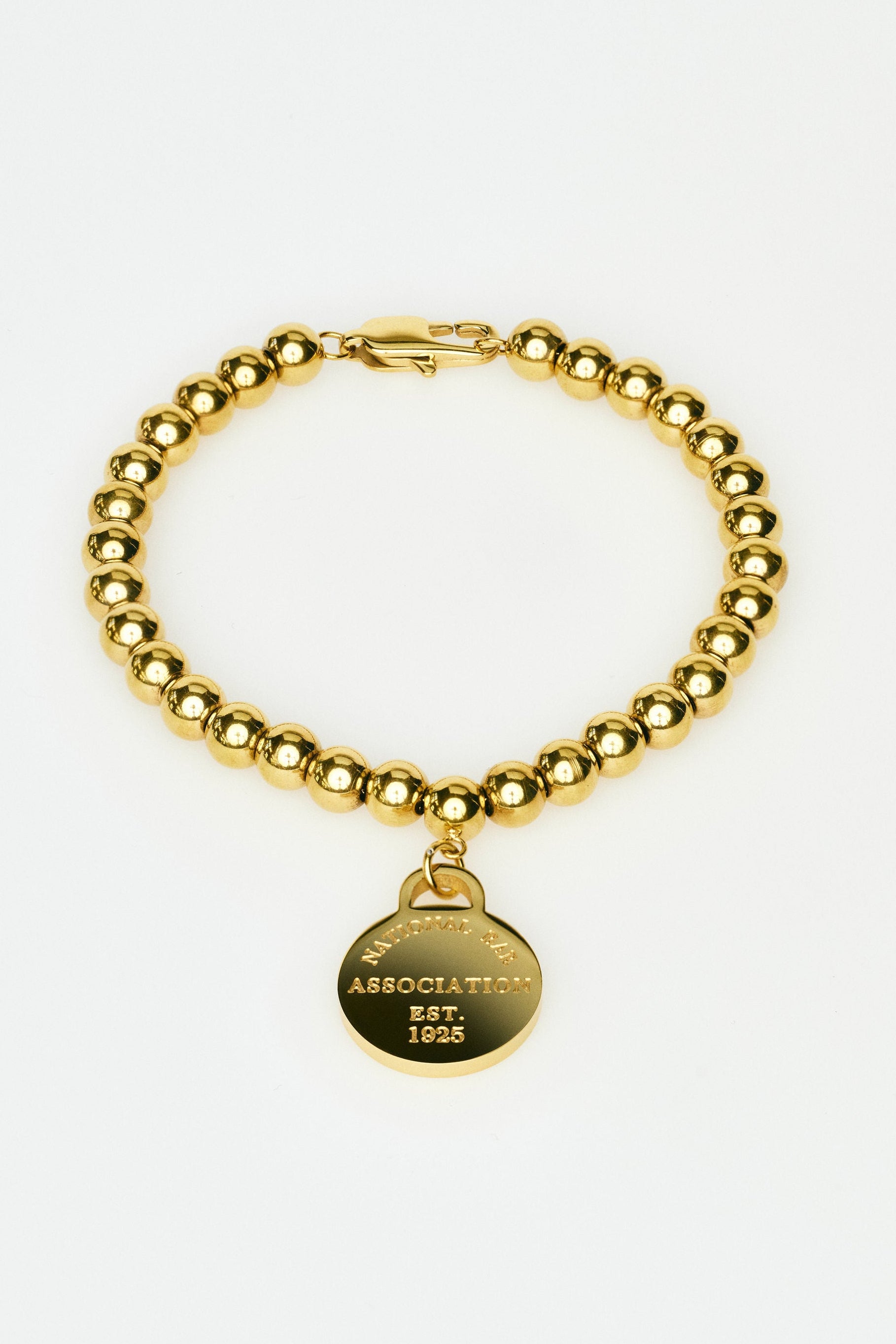 Gold beaded bracelet with a round tag on a white background