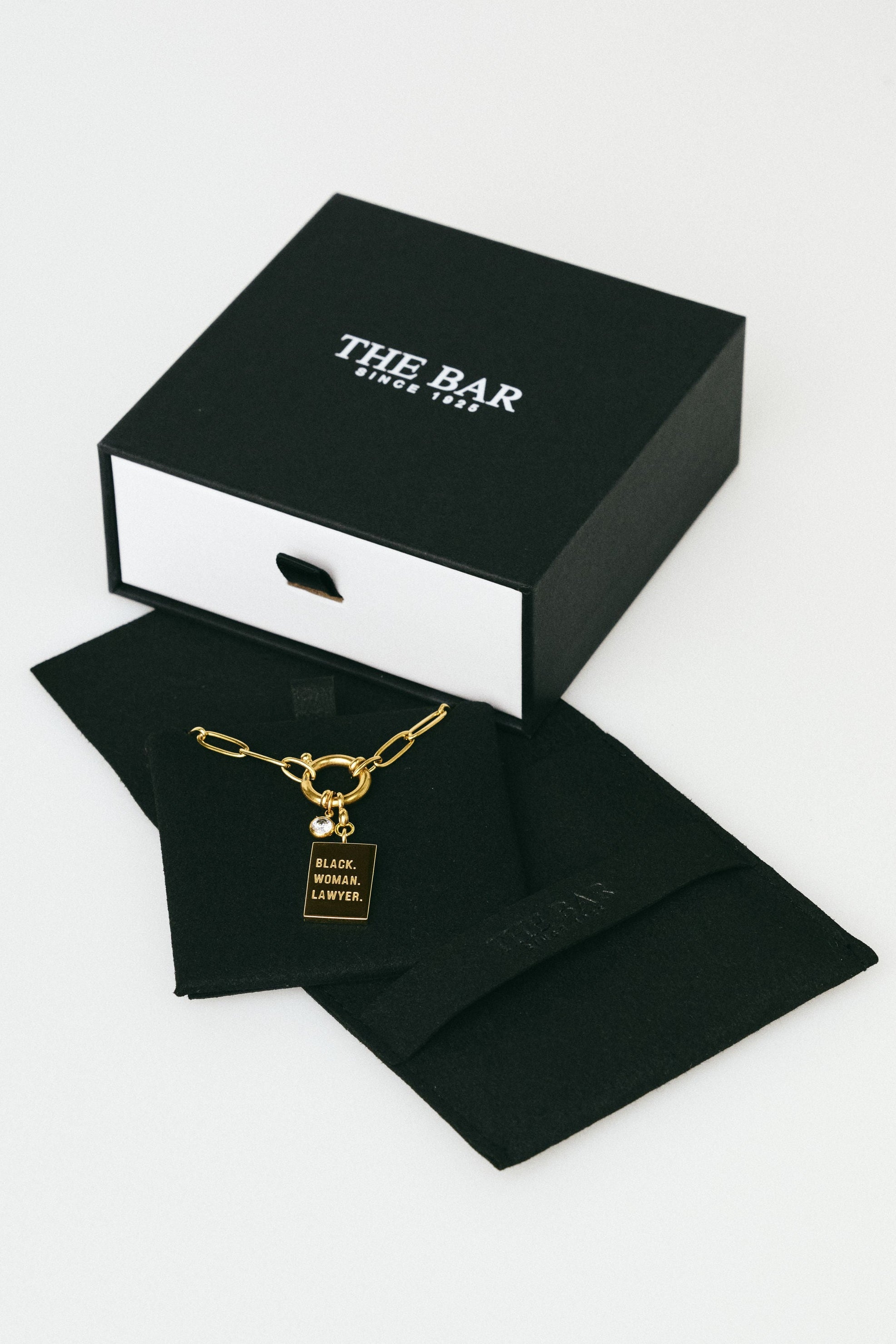 Gold necklace in a black box with 'The Bar' branding on a white background
