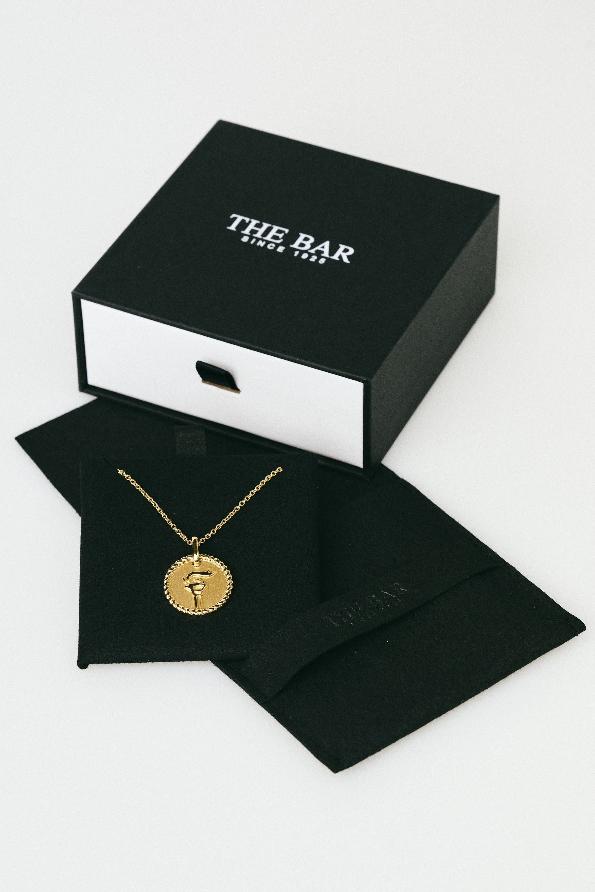 Gold necklace in a black box with 'The Bar' branding on a white background