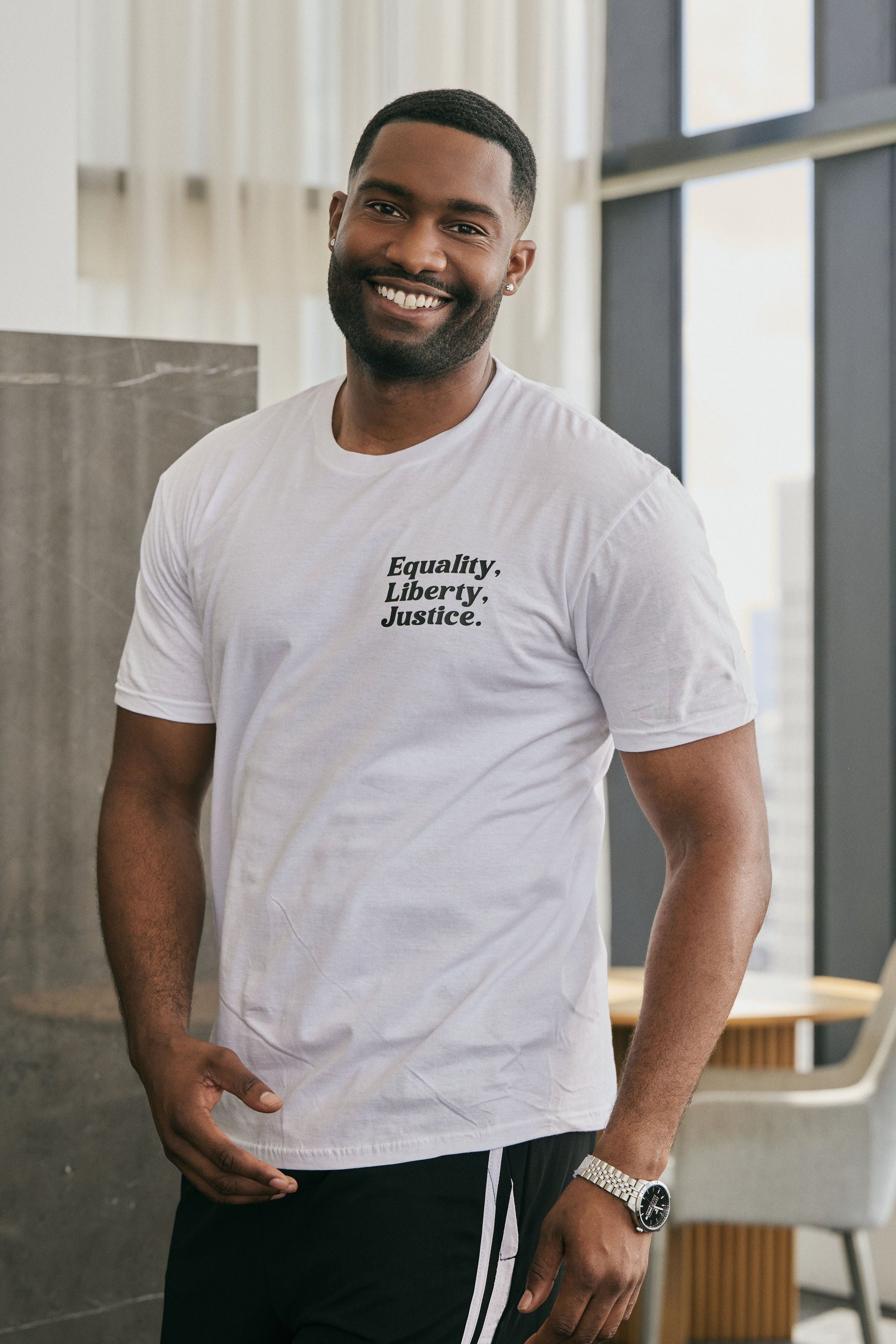 Man wearing a white t-shirt with a logo that reads 'Equality, Liberty, Justice.' on a neutral background