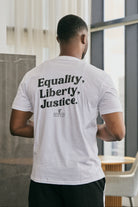Person wearing a white t-shirt with 'Equality, Liberty, Justice' text on the back in an indoor setting.