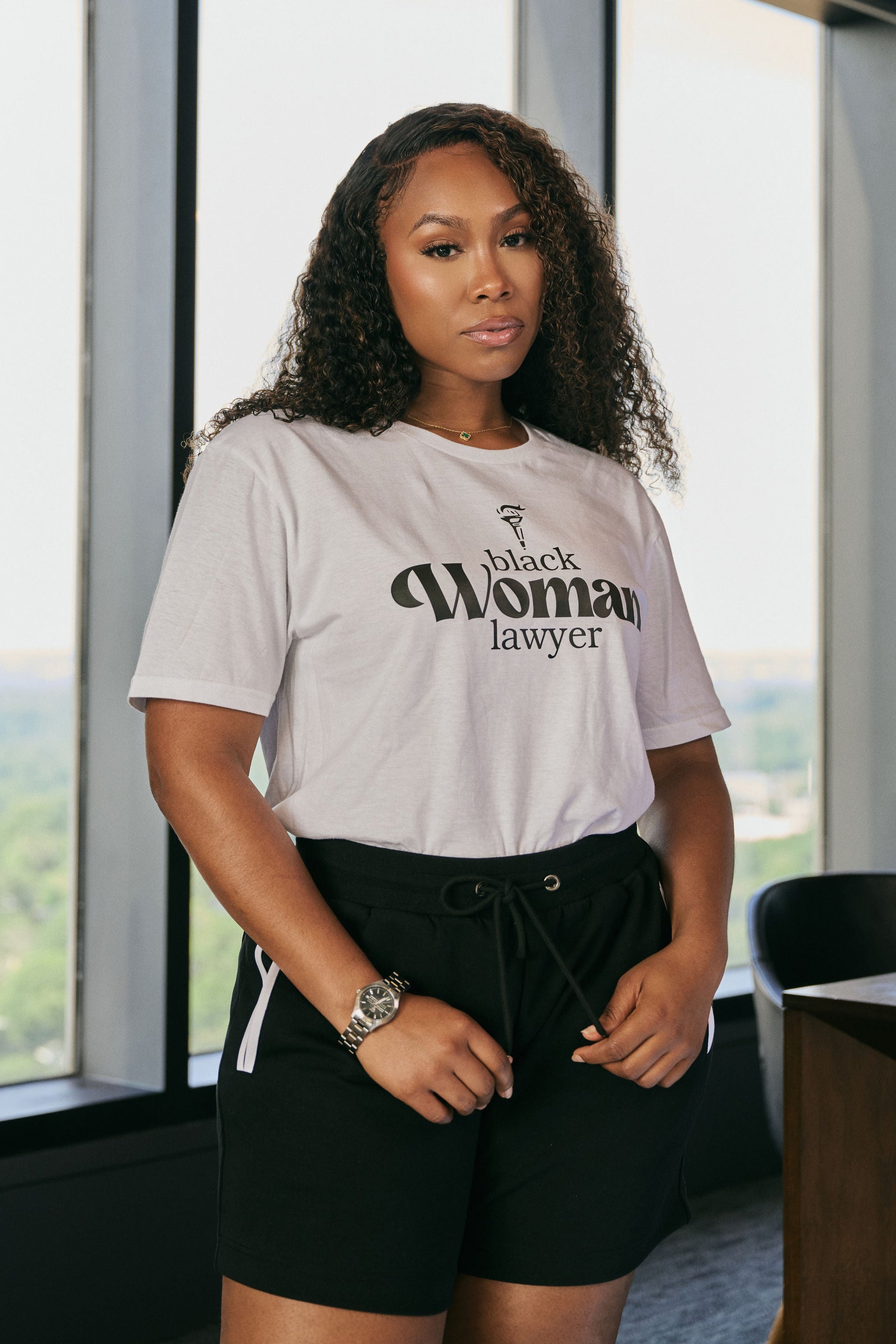 Woman wearing a white t-shirt with 'Black Woman Lawyer' text in an office setting