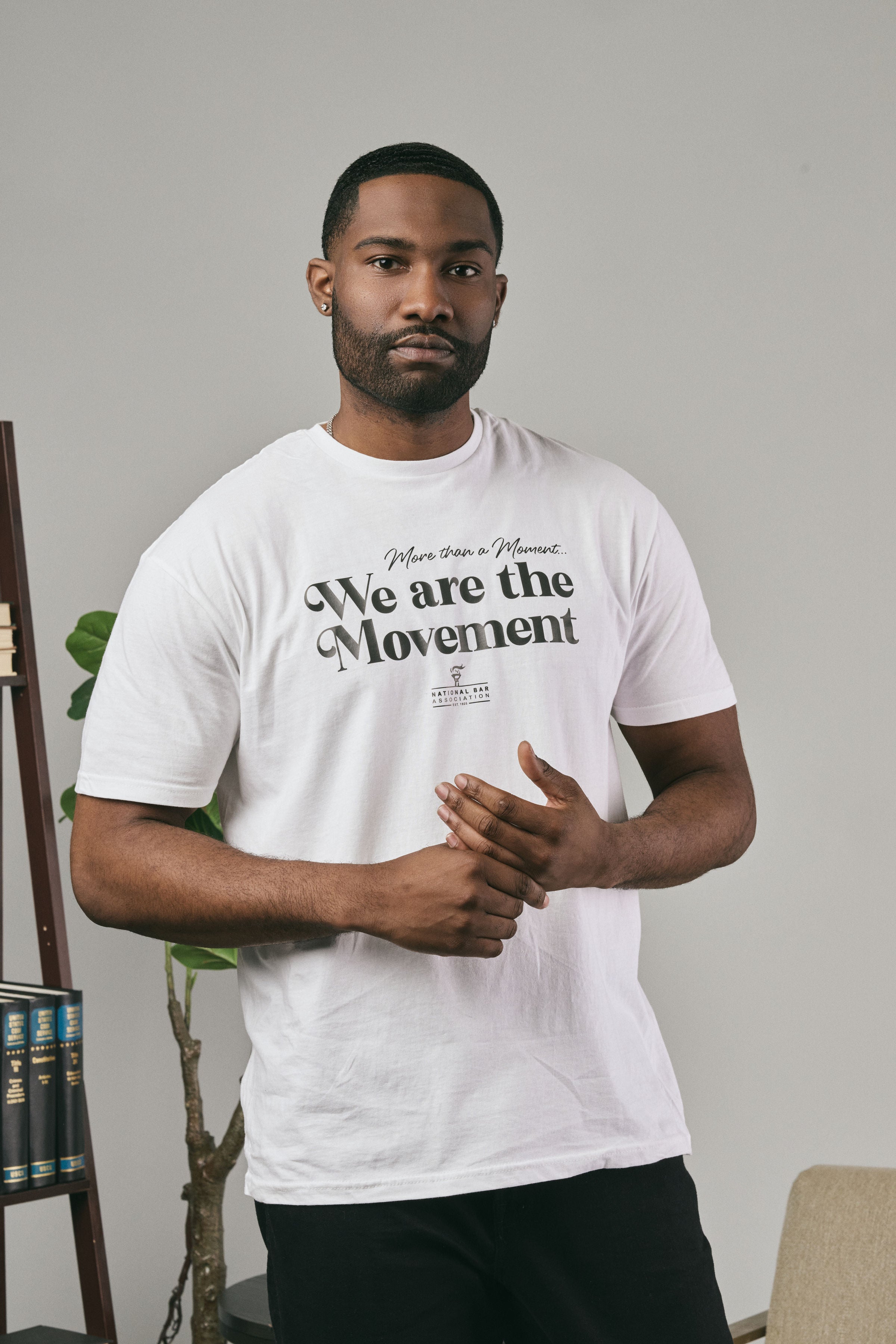 Man wearing a white t-shirt with 'We are the Movement' text, standing indoors.