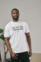 Man wearing a white t-shirt with text, standing indoors against a neutral background