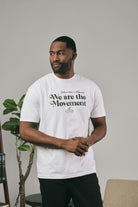 Man wearing a white t-shirt with text standing indoors and looking sideways against a neutral background