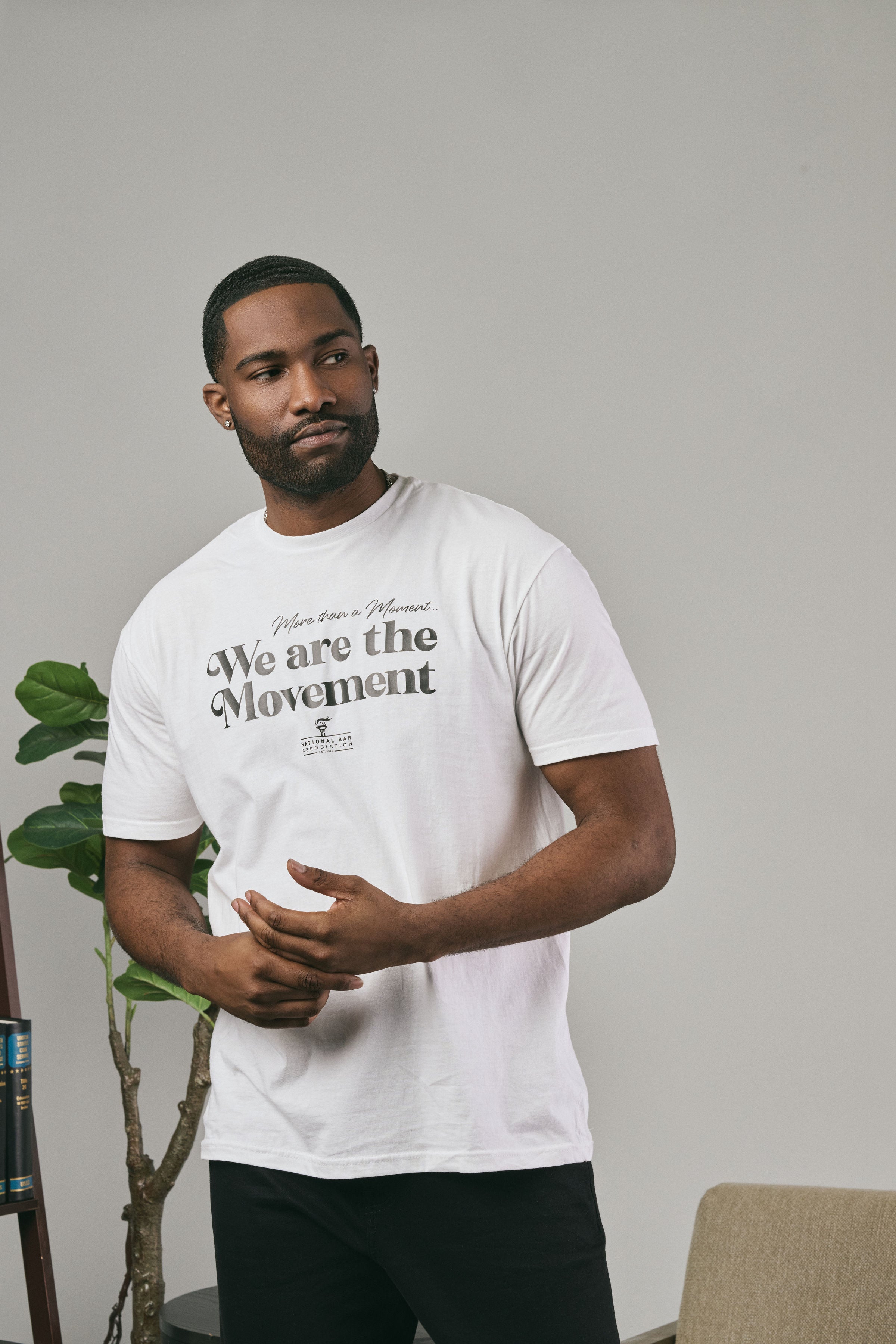 Man wearing a white t-shirt with 'We are the Movement' text, standing and looking sideways 
