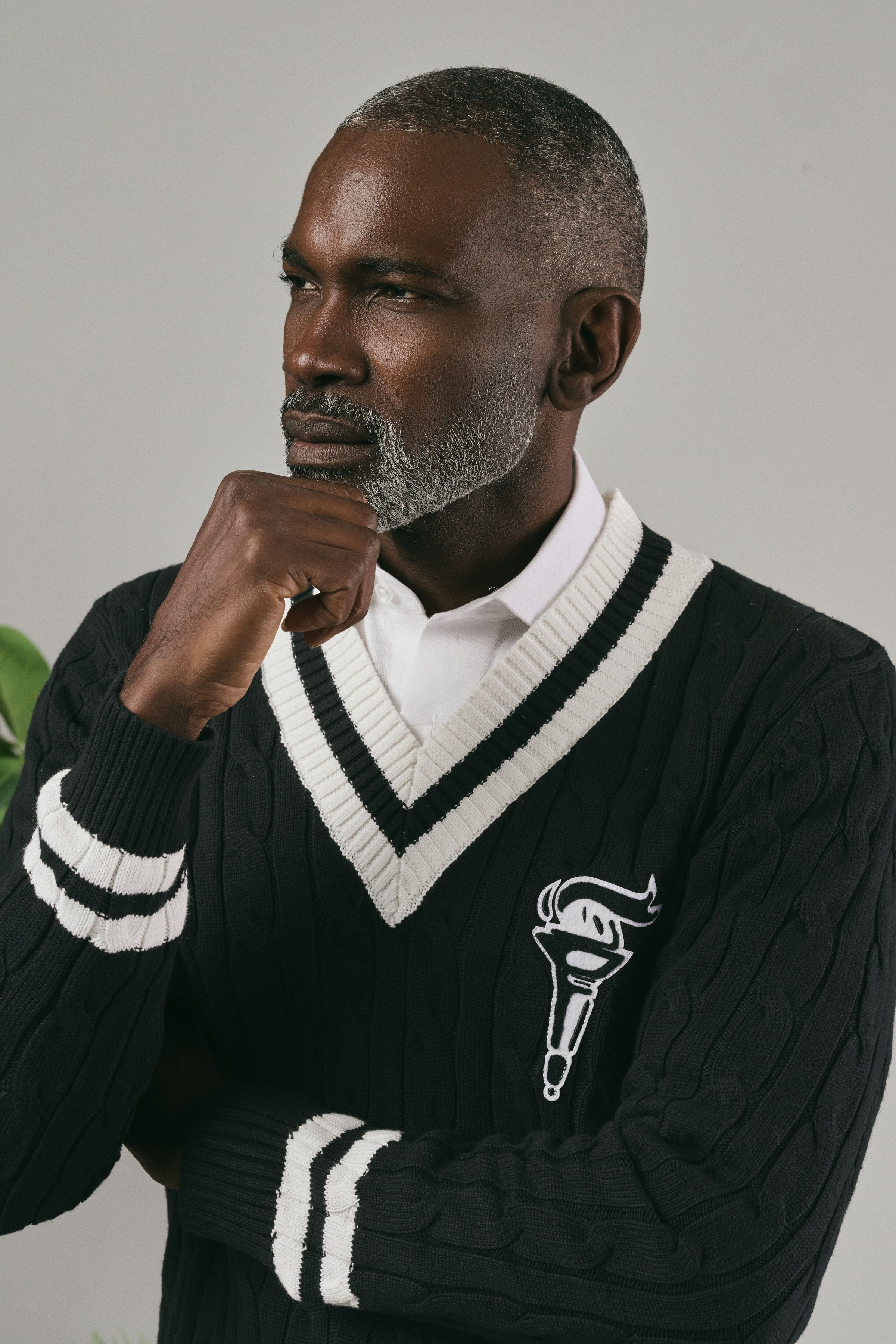 Man wearing a black sweater with white accents and a logo, posing against a grey background