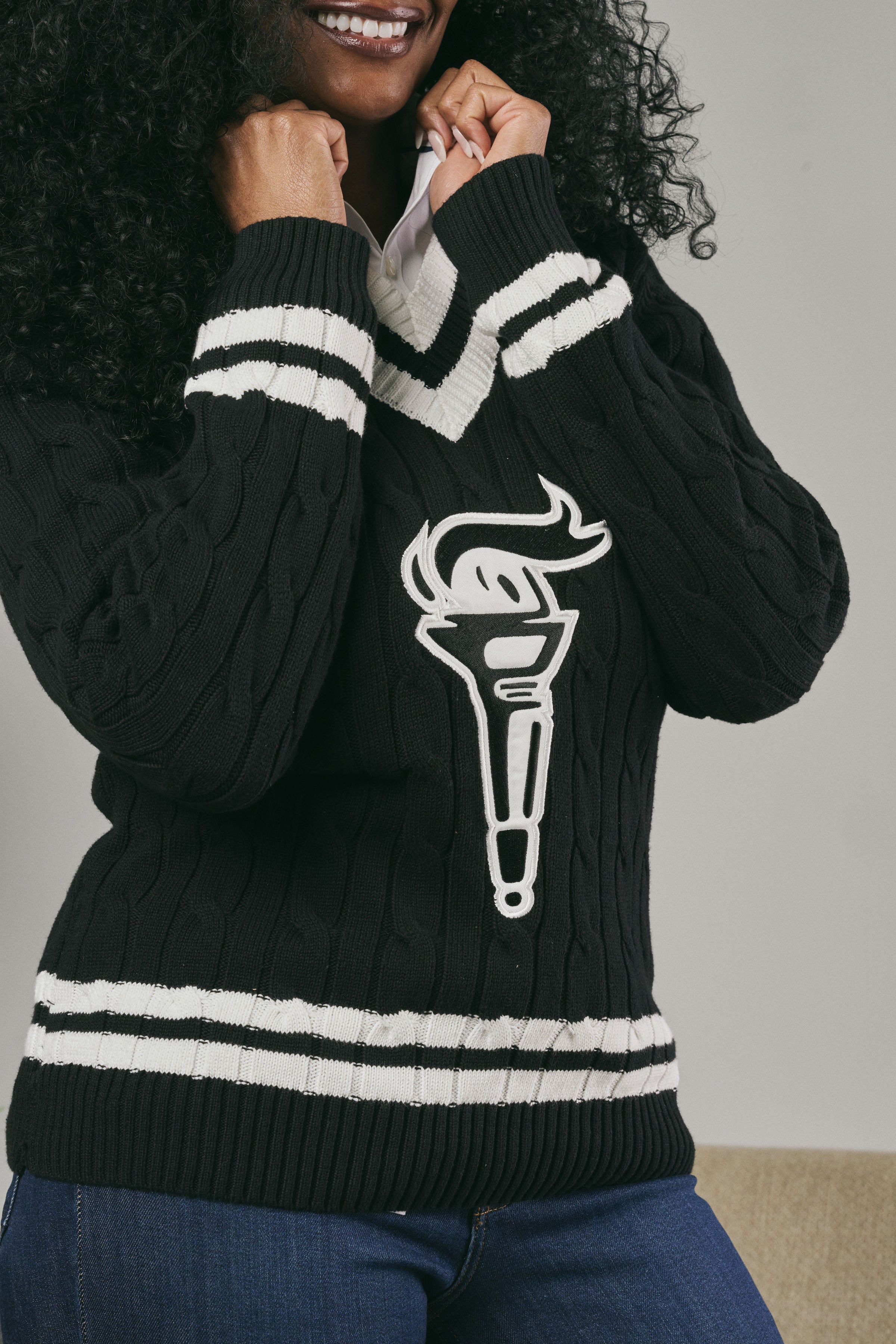 Person wearing a black sweater with a white emblem on a neutral background