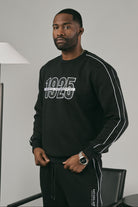 Man wearing a black sweatshirt with '1925' on it in an indoor setting.