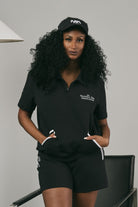 Woman wearing a black pullover and black shorts standing indoors.