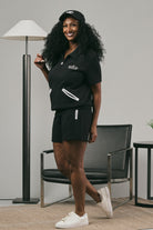 Woman wearing a black pullover and black shorts standing in a room with furniture and decor.