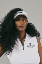 Woman wearing a white sleeveless polo with a logo and a white visor with 'NBA' branding.