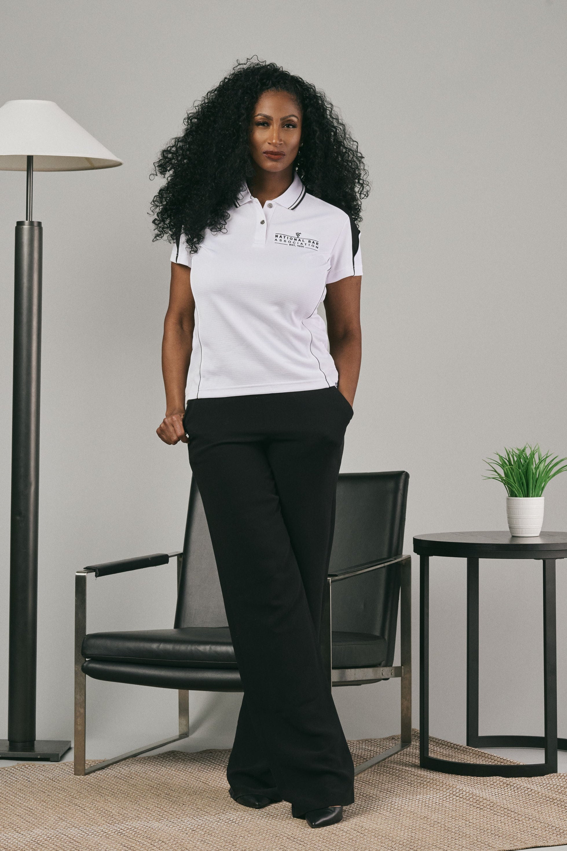 Woman wearing a white polo shirt with a logo in a minimalistic room.