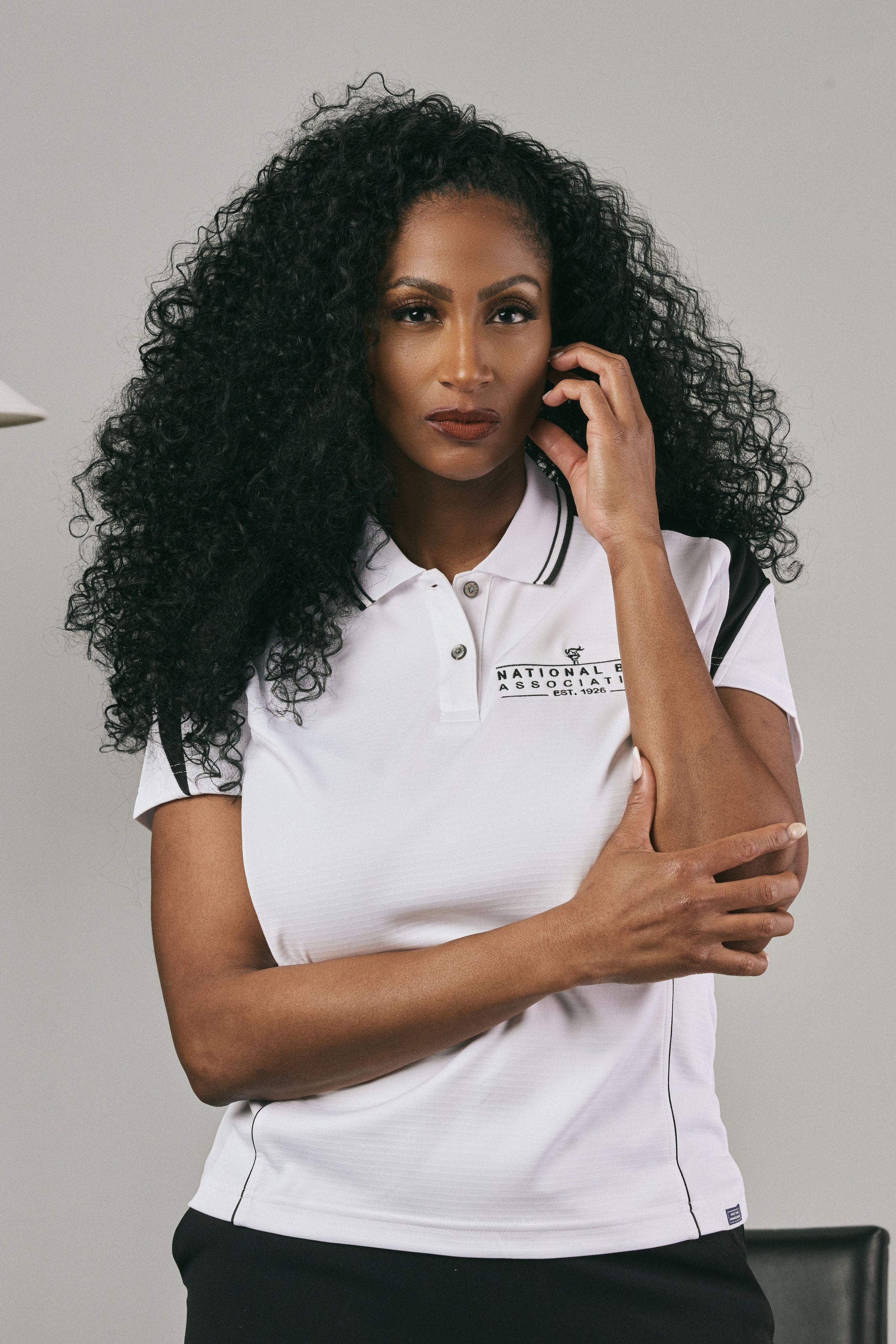 Woman wearing a white polo shirt with a logo, sitting against a plain background