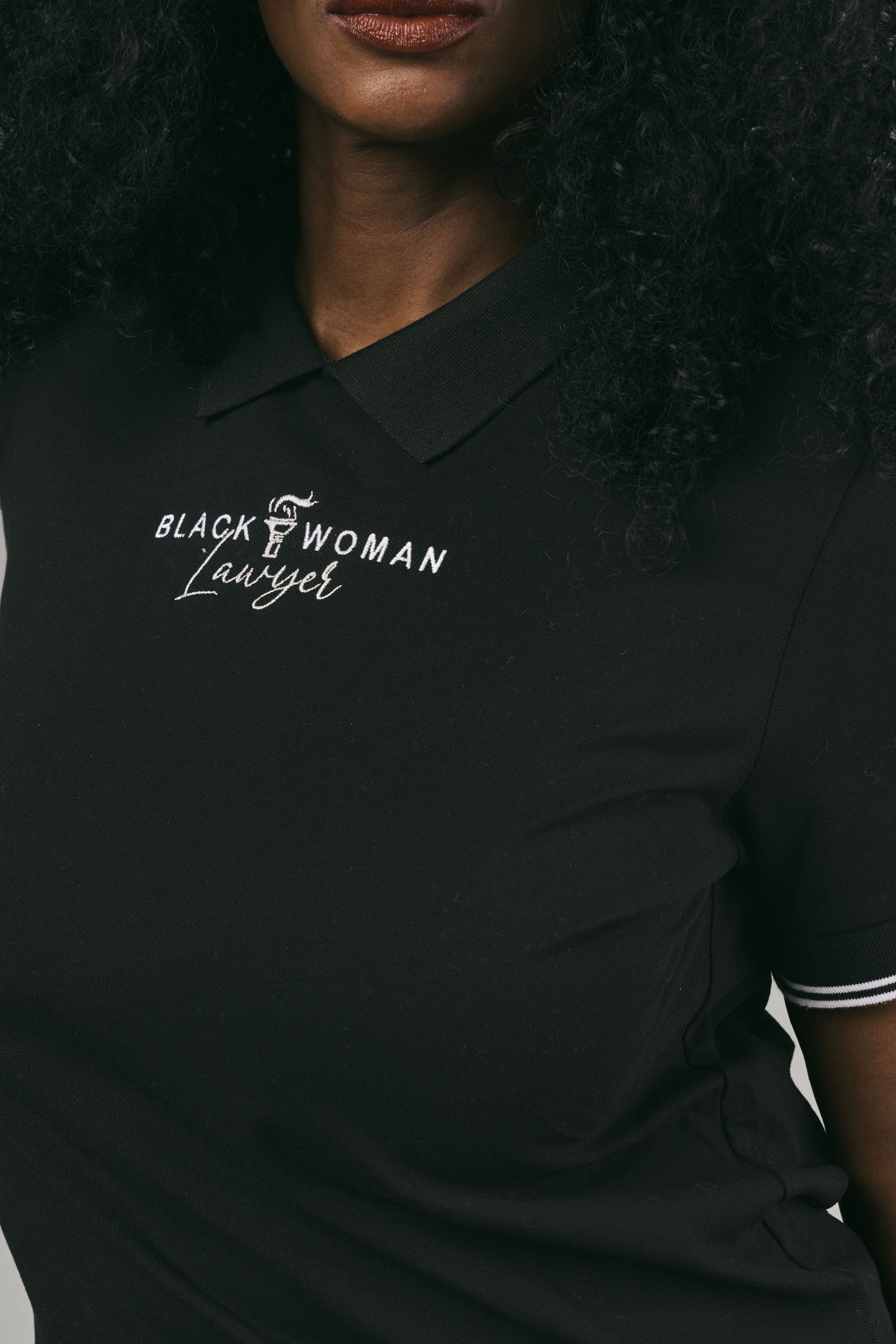 Black polo shirt with 'Black Woman Lawyer' text on a person wearing it.