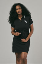 Woman wearing a black polo dress with a logo on a grey background