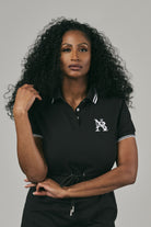 Woman wearing a black polo shirt with a logo on a grey background