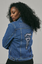Woman wearing a blue denim jacket with text and logo on the back against a grey background
