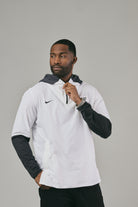 Man wearing a white jacket with a brand logo looking sideways against a grey background
