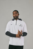 Man wearing a white and black jacket with a logo posing against a grey background
