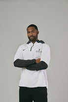 Man wearing a white and black jacket with a logo on a grey background