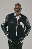 Man wearing a black and grey varsity jacket with visible branding on a grey background