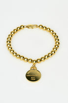 Gold beaded bracelet with a round tag on a white background