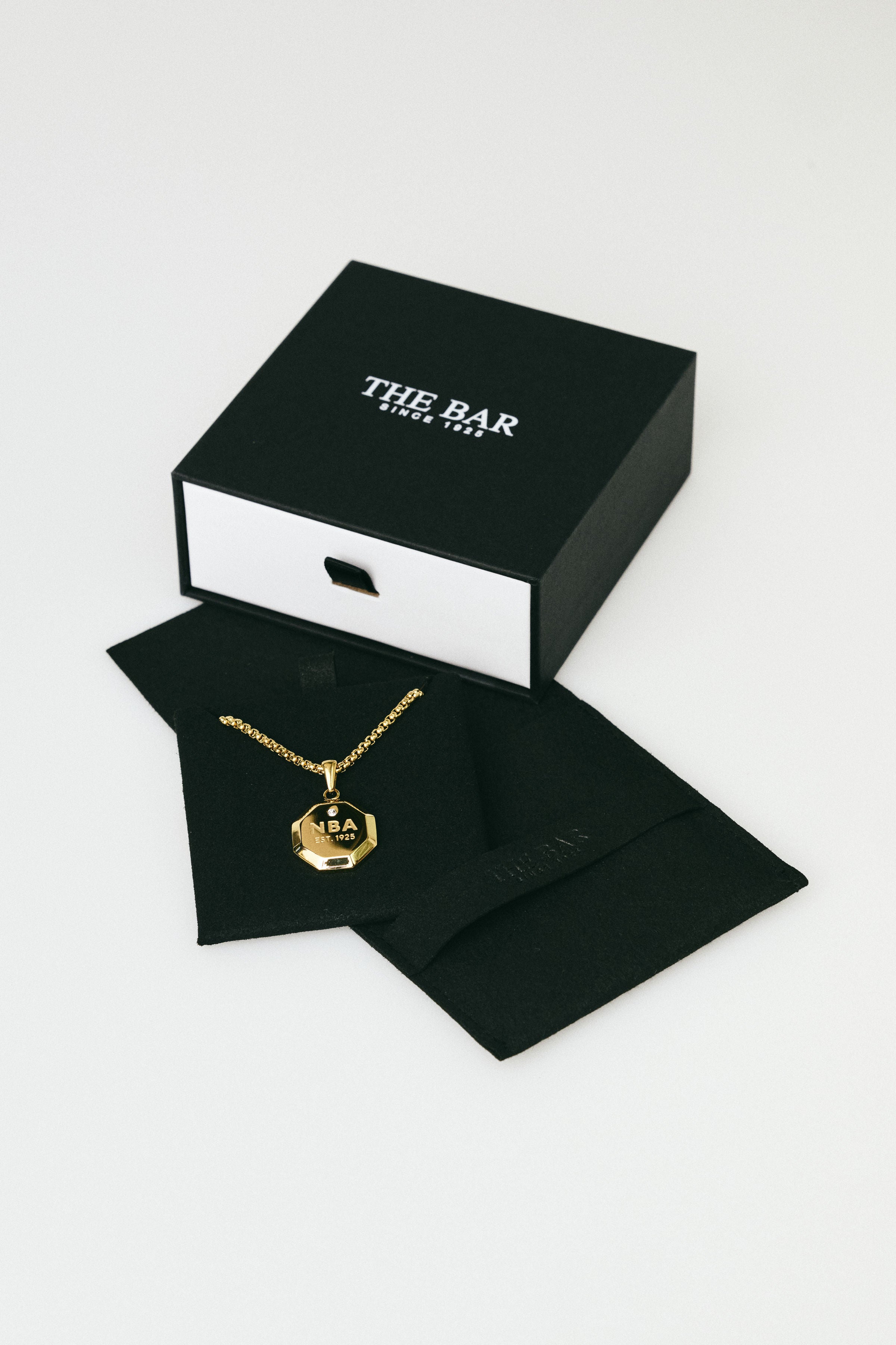 Gold necklace on black jewelry card with 'The Bar' box in the background