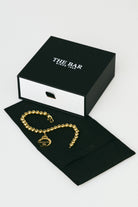 Gold bracelet on a black box with 'The Bar' branding on a white background